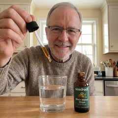 Man adding Seedroot Black Walnut Drops into a glass of water in his kitchen